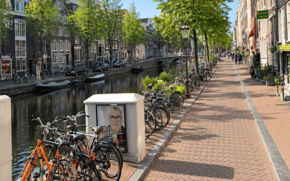 Rows of bicycles parked along an Amsterdam canal with fresh green trees in spring