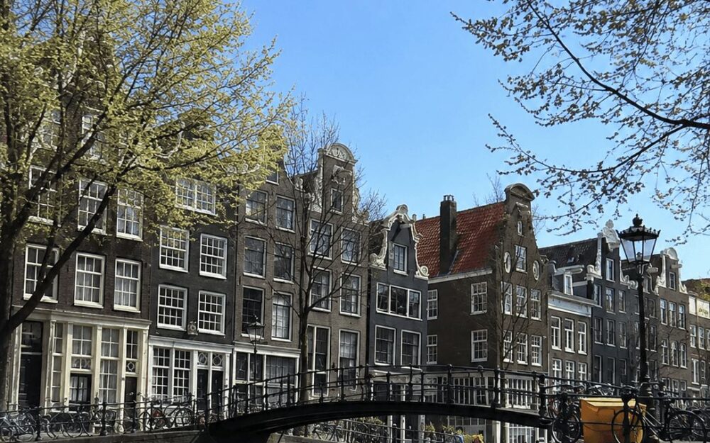 Small arched pedestrian bridge over an Amsterdam canal with gabled houses behind