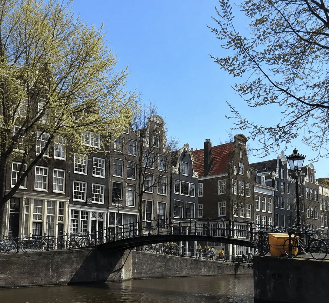 Small arched pedestrian bridge over an Amsterdam canal with gabled houses behind