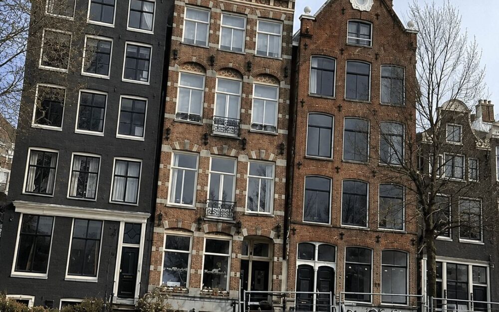 Three adjoining Amsterdam canal house facades seen from a boat on the water