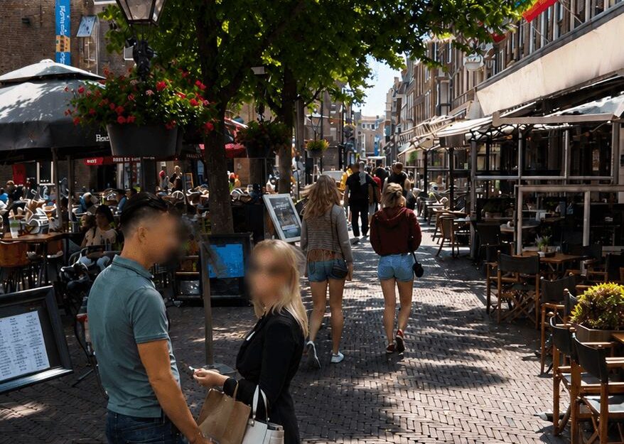 Amsterdam pedestrian street with café terraces, hanging flowers and rainbow pride flags in summer