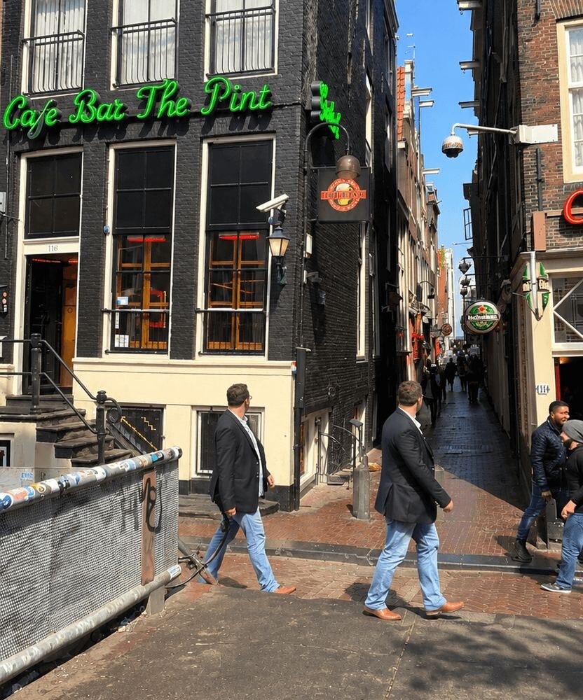 Pedestrians walking along a narrow Amsterdam street lined with tall brick buildings and bars
