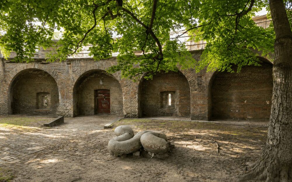 Brick archways and courtyard of a historic Dutch fortification shaded by a large tree
