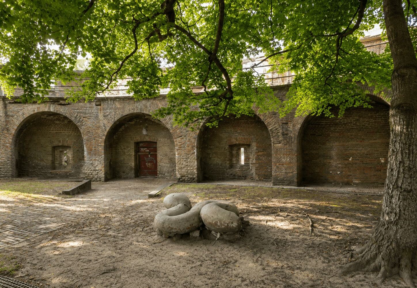 Brick archways and courtyard of a historic Dutch fortification shaded by a large tree