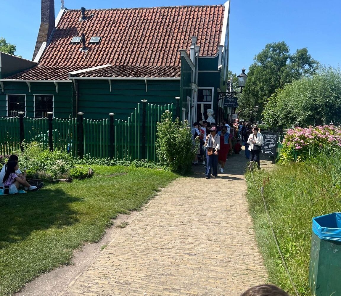 Family walking along a path between green wooden buildings at Zaanse Schans
